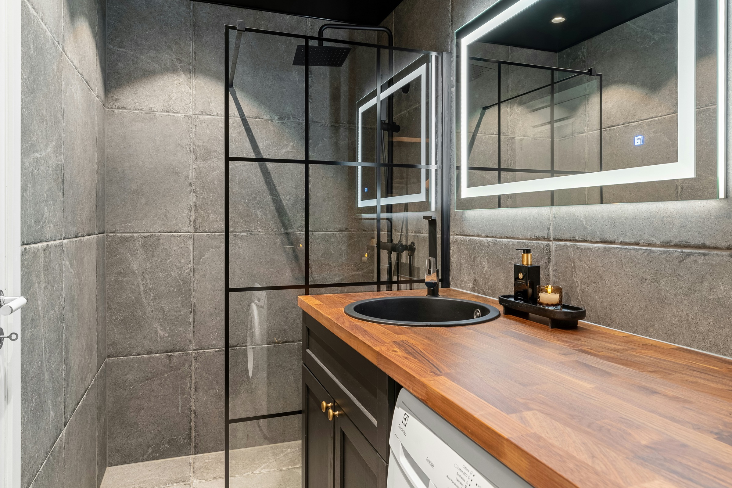 Dark walk-in shower with illuminated mirrors and black fittings
