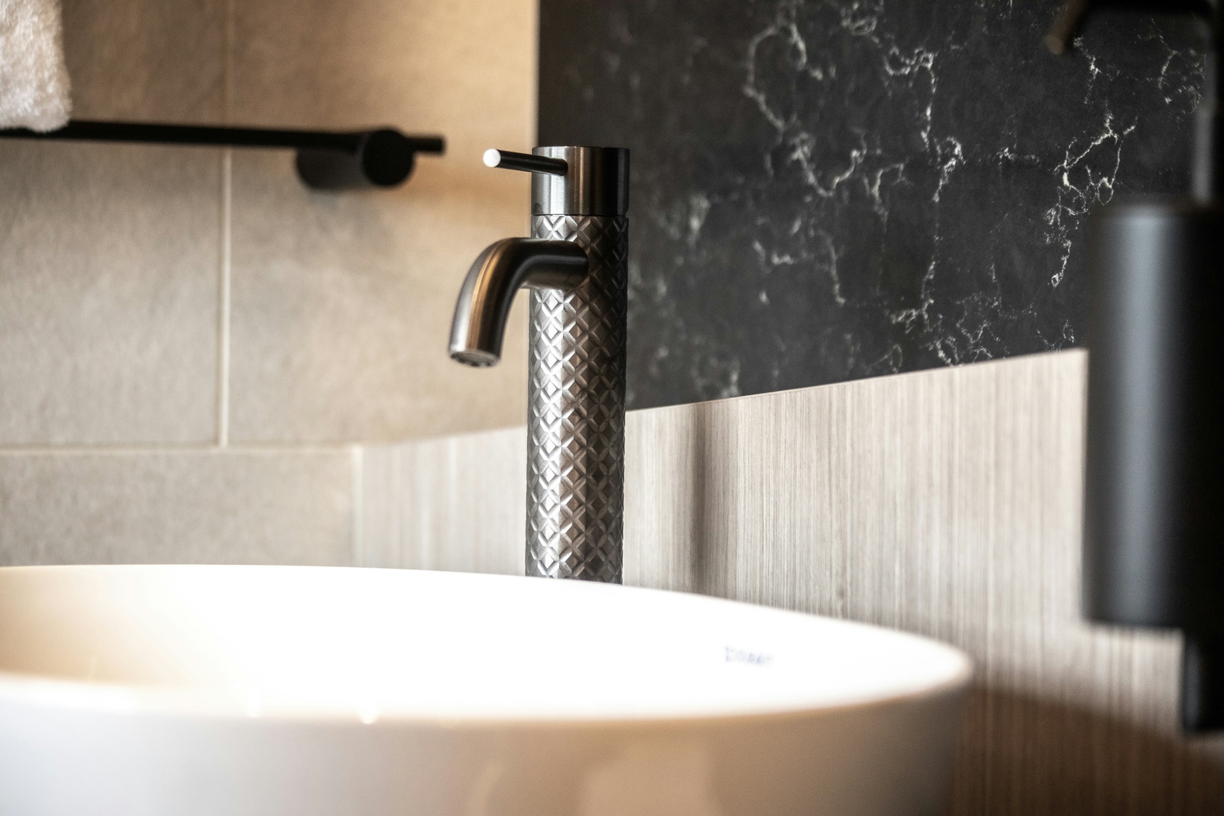 Close-up of a premium basin faucet against dark stone and soft wall finish